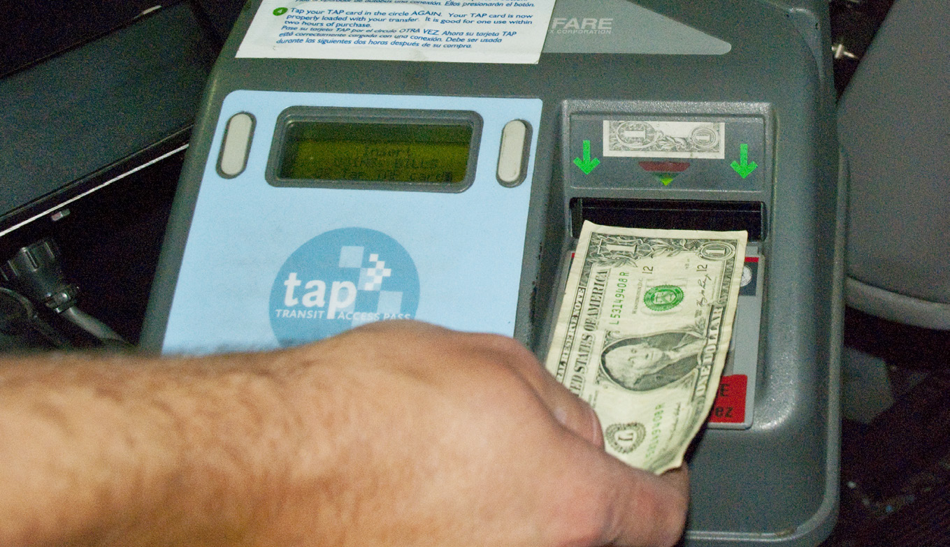 a hand inserts a dollar bill into the slot on a fare box