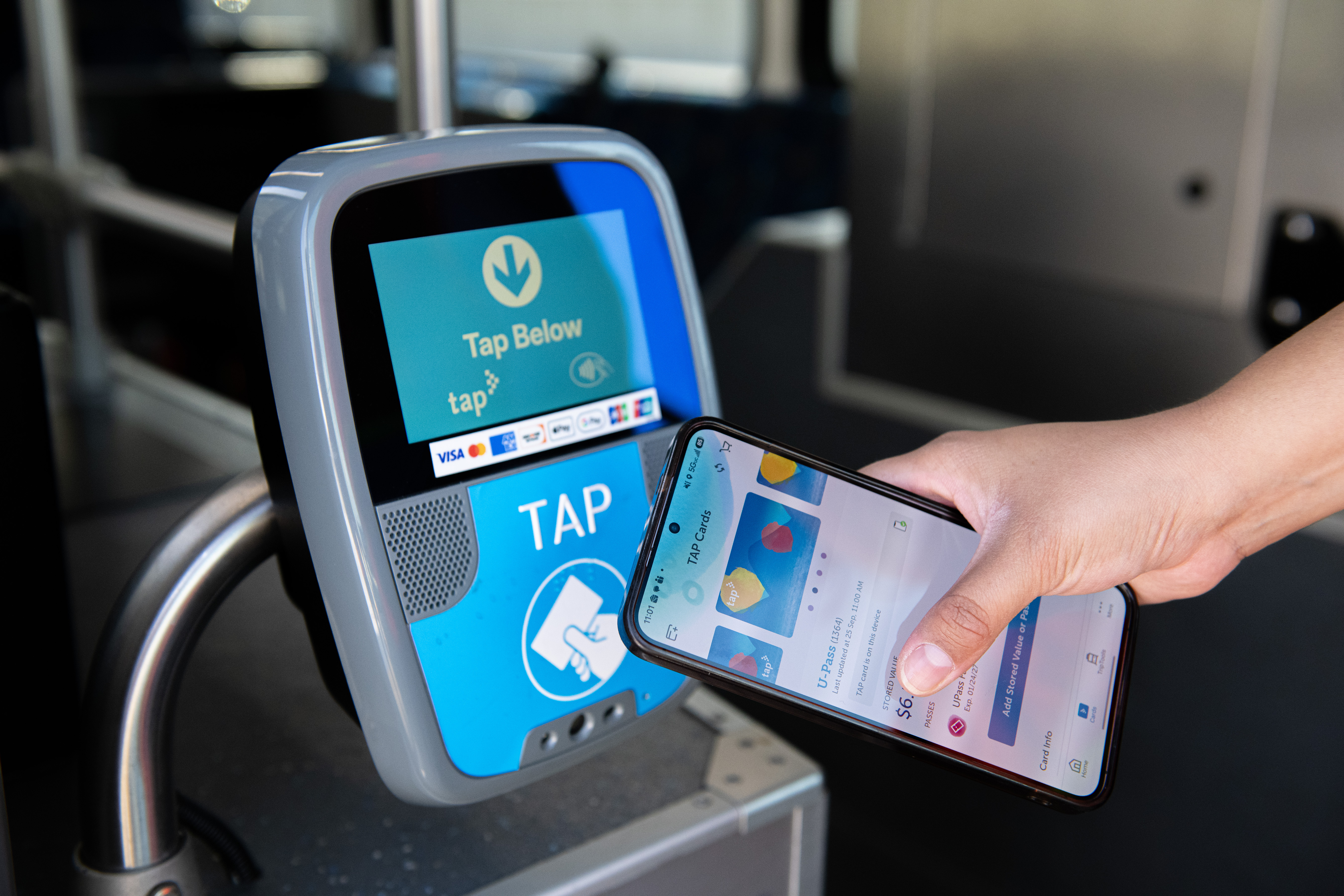A hand taps a phone against the small TAP validator by the bus door
