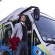 Smiling customer gets off bus holding roses.