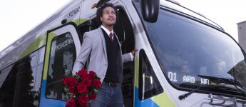 Smiling customer gets off bus holding roses.