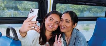 Two customers share a smiling selfie on board a bus.